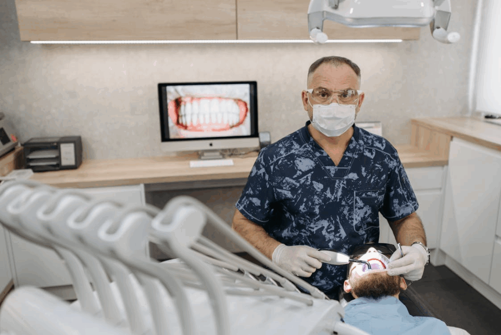 a photo showing a detist working on a patient with an image of teeth on the screen behind him