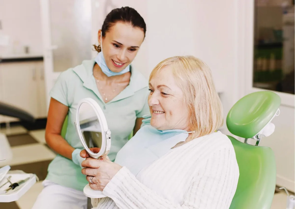 Dental professional helping an older patient view her smile after receiving partial dentures.
