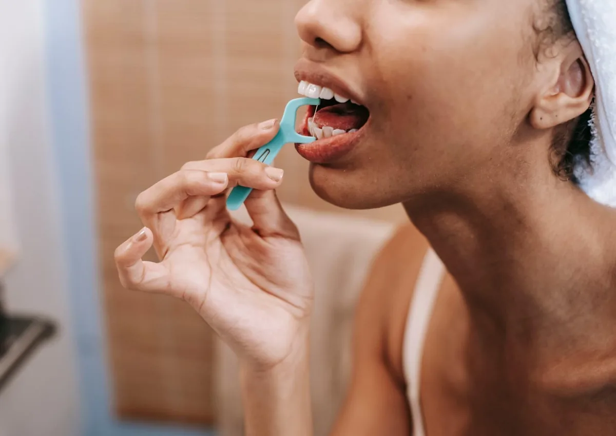 Woman using dental floss to remove plaque between her teeth as part of a routine oral hygiene and dental cleaning regimen.